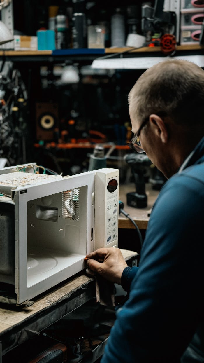 An adult male fixing a microwave in a cluttered workshop, focusing on repairs.